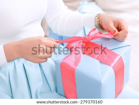 Time to open presents. Close up hands of a girl pulling a red ribbon to open her birthday gift in a blue box