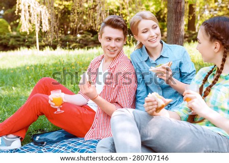 Three friends. Three young people holding glasses with soda and sandwiches during picnic.