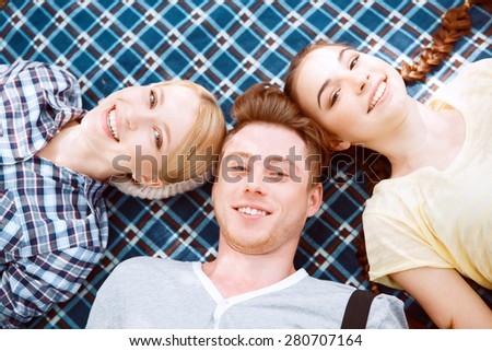 Head to head. Top view of guy and two girls lying on blue cover.