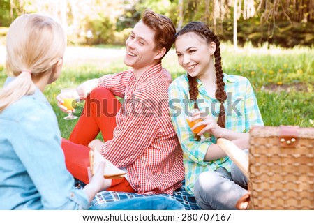 Funny picnic. Three beautiful young people with soda and sandwiches during picnic in park.