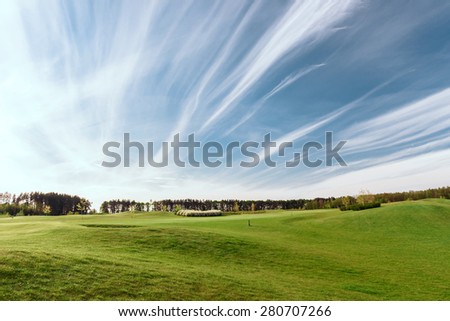 Breath taking. Beautiful landscape with green field, trees and sky with stripy clouds.