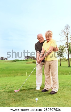 Teaching with love. Old man standing on course behind his wife and teaching her to play golf