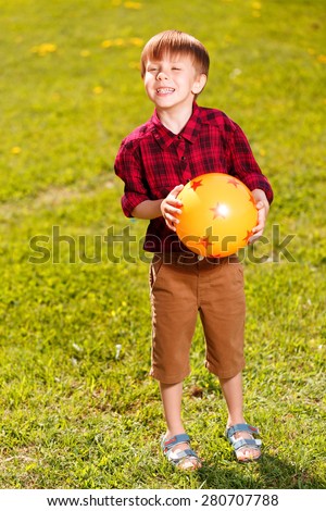 Ready to play. Little smiling boy holding rubber ball and standing on grass field.