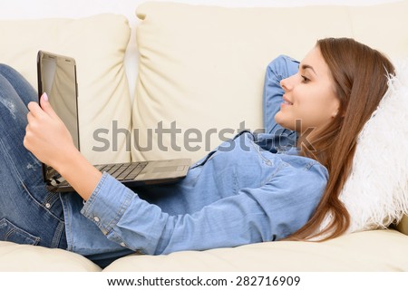 Free day. Girl lying on sofa  and watching films at laptop
