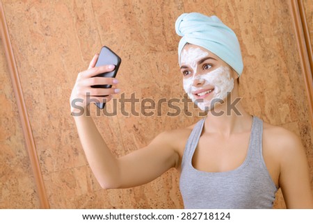 Funny selfie. Girl doing selfie with white clay beauty mask on face.