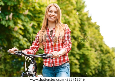Portrait of a young beautiful blond girl standing near her mountain bicycle posing and smiling ,wearing a red checkered shirt  in a green park