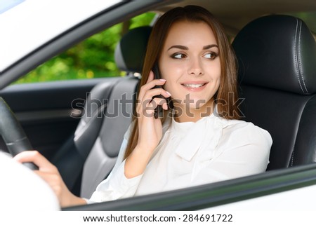 Being busy. Pretty young lady driving new car and talking per mobile phone.