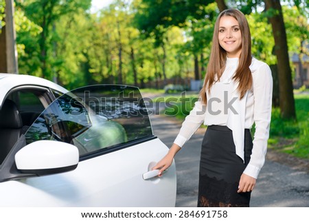 Getting ready. Portrait of young smiling lady standing near car and opening door.