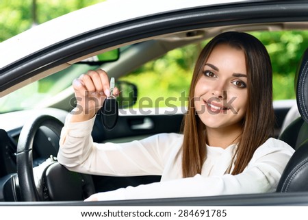 Look what I have. Young smiling beautiful woman sitting inside car and holding key in her hand.