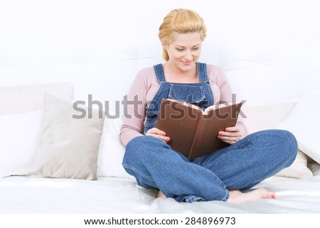 Touching story. Pregnant young woman reading book and smiling while relaxing and reading book on the couch.