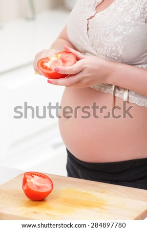 Bright cooking. Pregnant young woman cleaving tomato while cooking healthy salad in the kitchen.