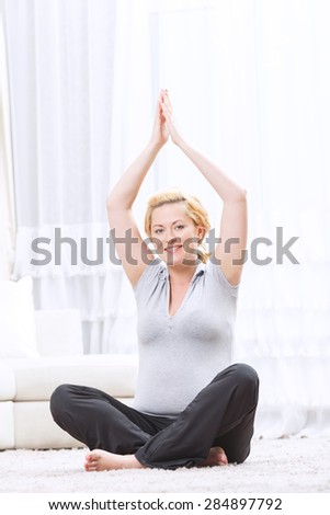 Keep your body healthy. Pregnant young woman practicing physical exercises and keeping her hands up in the air whole sitting.
