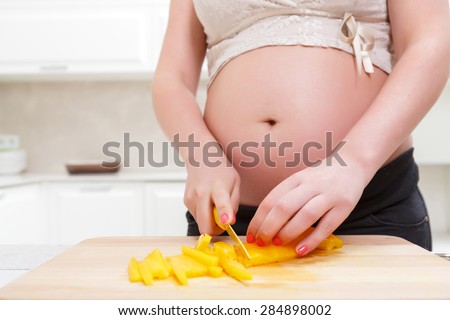 Tasty dinner. Pregnant woman cutting vegetables and preparing  healthy and tasty food while standing in the kitchen.