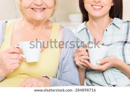 Smiling together. Portrait of young and old smiling women holding cups of tea