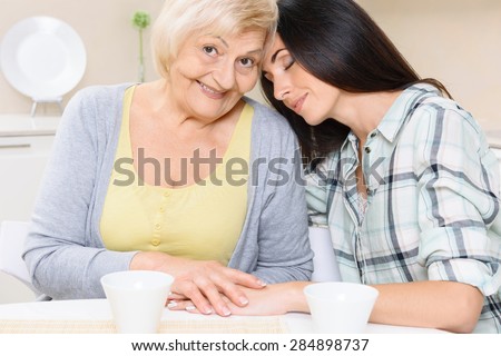 Family union. Pretty young woman leaning on shoulder of her granny in kitchen.