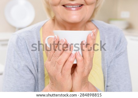 Five o clock tea. Close up of smiling old woman sitting in kitchen and holding cup of tea.