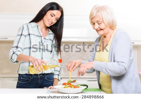 Working together. Two women of different generations standing in kitchen and cooking salad.
