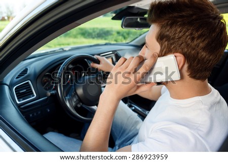 Doing forbidden things. Young man with beard .driving car and talking per mobile phone