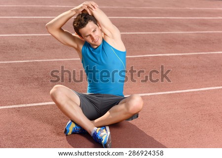 Stretch higher. Handsome young sportsman sitting and holding his arms behind while stretching