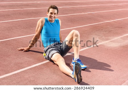 Having rest. Young smiling sportsman sitting on floor and having rest.