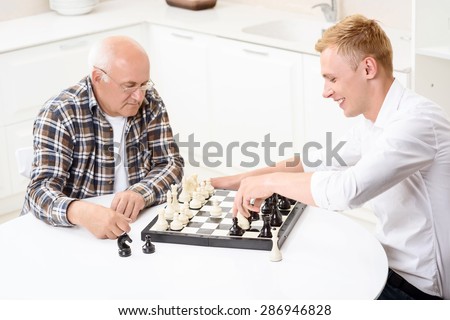 Ready to start. Grandson and grandfather sitting together in kitchen and going to play chess