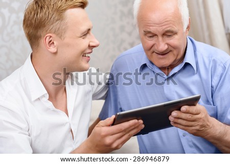 Showing news. Grandson showing his new photos on tablet to his grandfather