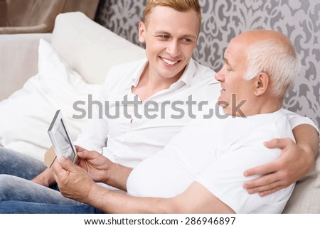 Old years. Grandfather and grandson sitting on sofa and holding photo in frame