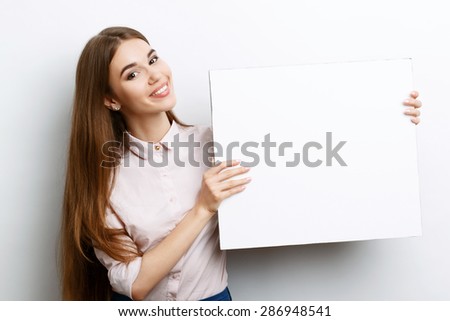 Portrait of a young beautiful girl with long brown hair wearing pink cotton blouse, standing waist up smiling and holding a copy space in her hands charming , on a white background