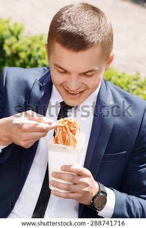 So tasty. Youthful businessman eating Chinese noodle soup outside with great enthusiasm