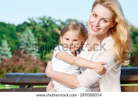 Giving care. Young attractive mother sitting in park and holding her little cute daughter