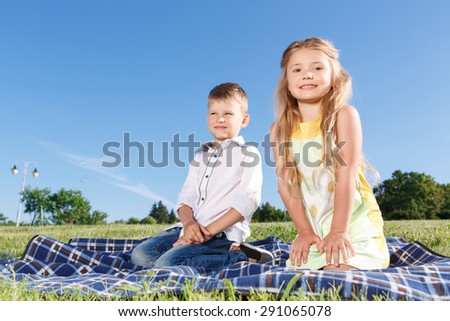 Enjoy the moment. Nice little children holding their  hands down and sitting on  blanket while evincing positive emotions.
