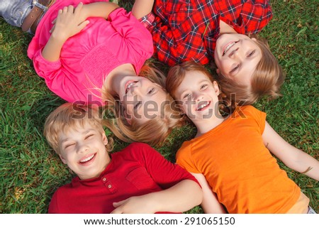 Enjoying time. Funny children lying in raw on the ground  and smiling while expressing positivity.