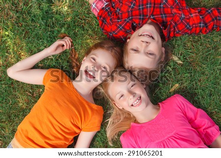 Hey. Cheerful smiling  friends lying on the green grass and having fun in the yard.