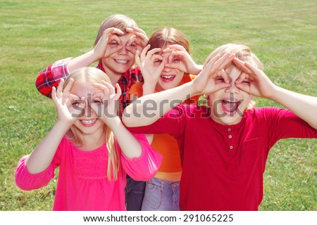 We see you. Nice pleasant children holding their hands on faces imitating binoculars while smiling and having fun in the yard.