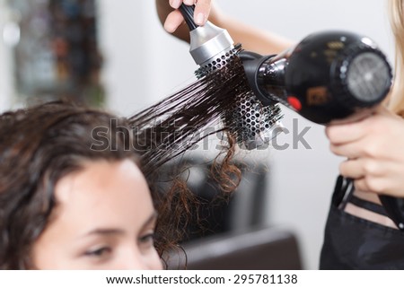 Make it dry. Selective focus of hair rolled on comb in hands of professional hairdresser holding hairdryer and making hairstyle.