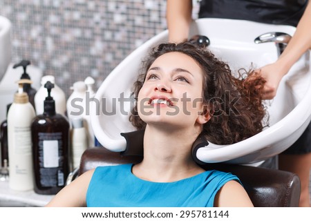 Good feeling. Close up of attractive young lady leaning her head backwards and smiling while having  hair washed in beauty salon