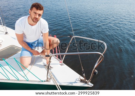 Last minute adjustments. Top view of upbeat man standing on one knee and adjusting the yacht while going to sail.