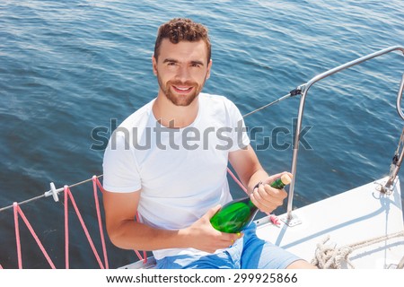 Lets make fun.  Top view of vivacious handsome man holding bottle of beverage and looking up while opening it on the yacht