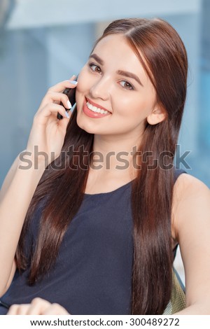 Pleasant conversation. Nice young business woman holding mobile phone and talking on it while expressing joy.