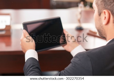 Follow new technologies. Selective focus of nice lawyer holding laptop and sitting at the table while being busy at work
