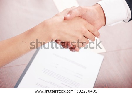 Come to agreement. Close up of nice colleagues shaking hands with document lying on the table in background