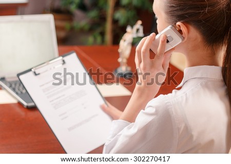 Addicted to work. Pleasant woman talking on phone and holding documents while being busy at work.