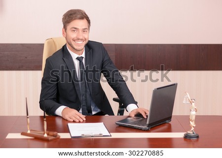 Love my job. Upbeat handsome man sitting at the table and smiling while being busy at work
