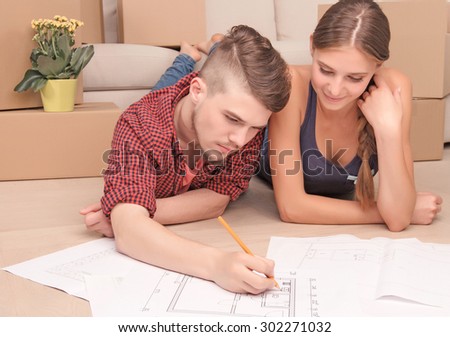 Serious project. Pleasant thoughtful young husband lying on the floor and making plan together with his wife.