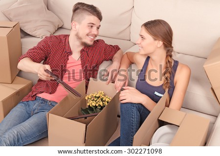 Take it. Upbeat smiling young couple sitting on the floor and unpacking boxes while evincing joy.