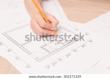 Real engineer. Close up of young husband holding pencil and making drawings of his new flat on the floor