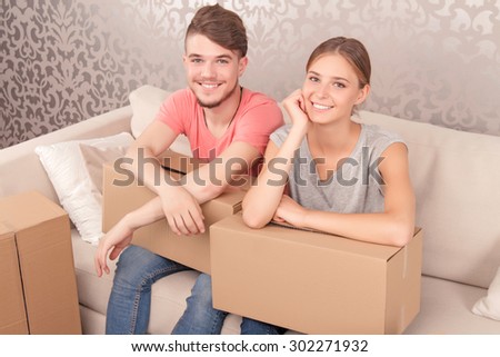 Feeling elated. Content young couple sitting on the couch and holding boxes on knees while expressing joy.