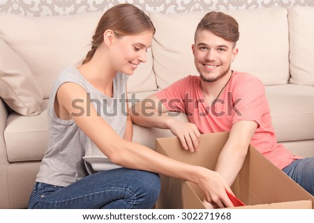 Feeling over the moon. Nice smiling young couple sitting on floor and leaning against settee while unpacking boxes