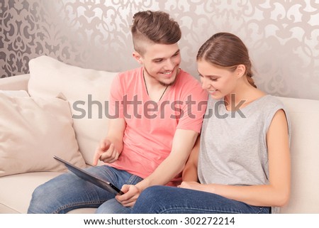 Do you like it. Overjoyed young couple sitting on holding laptop and smiling while sitting on the settee