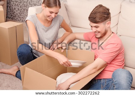 So many plates. Euphoric cheerful young couple sitting on the floor and smiling while unpacking boxes.